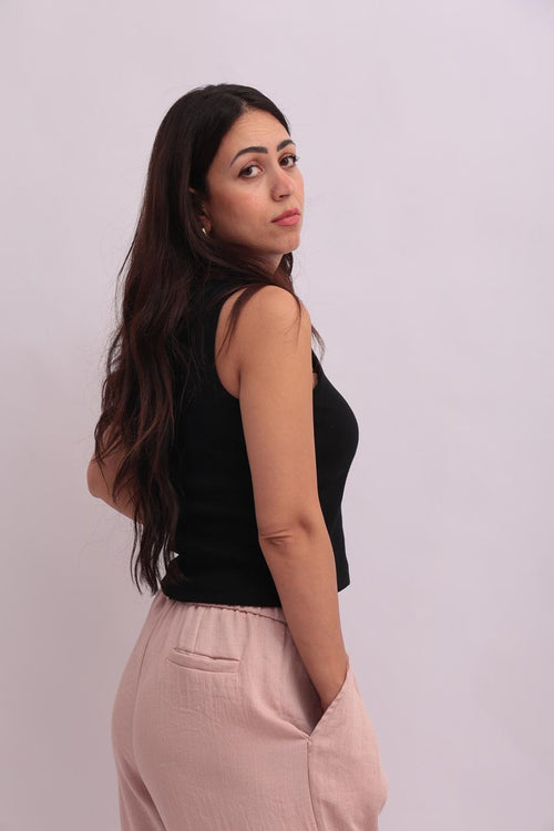 Model wearing a black cropped tank top styled with high-waisted pink trousers, showing the back and side view of the minimalist design.
