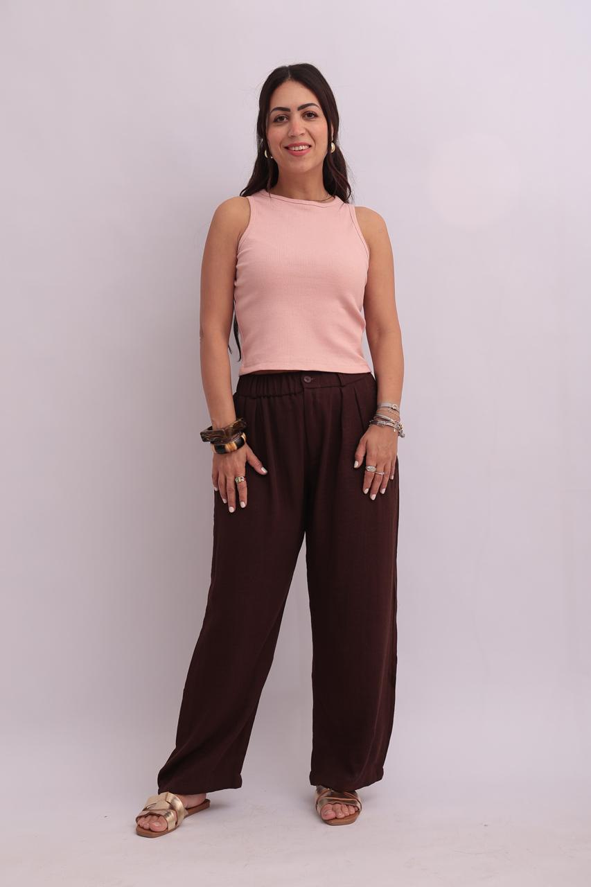Full-body shot of a model styling a light blush pink ribbed tank top with relaxed-fit chocolate brown trousers, completing a modern minimalist look.