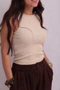 Close-up shot of a model wearing a cream-colored ribbed crop tank top, paired with dark brown wide-leg trousers.