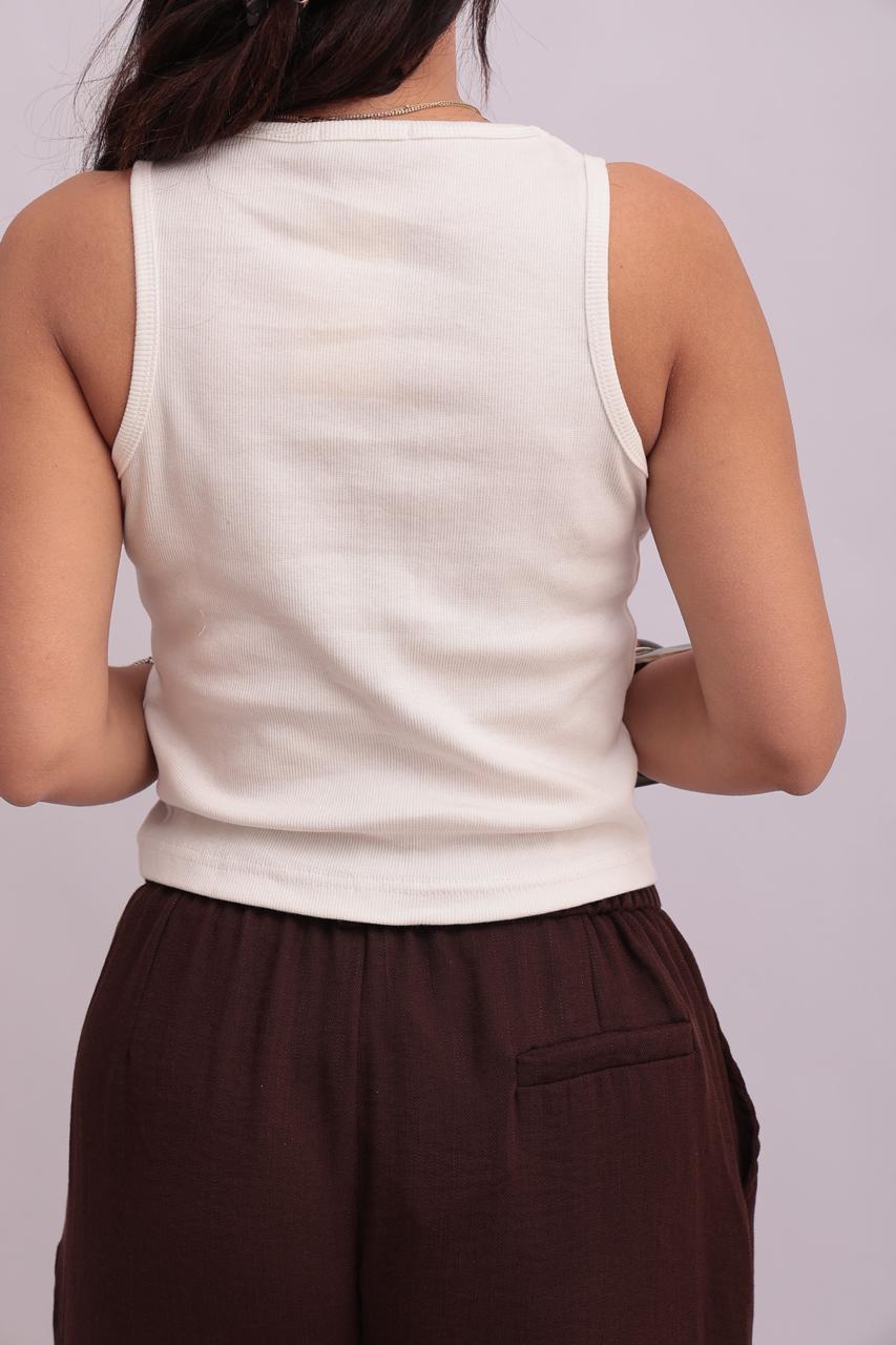 Back view of a model wearing a white ribbed crop tank top and dark chocolate brown trousers, showcasing the clean armholes and neck binding.