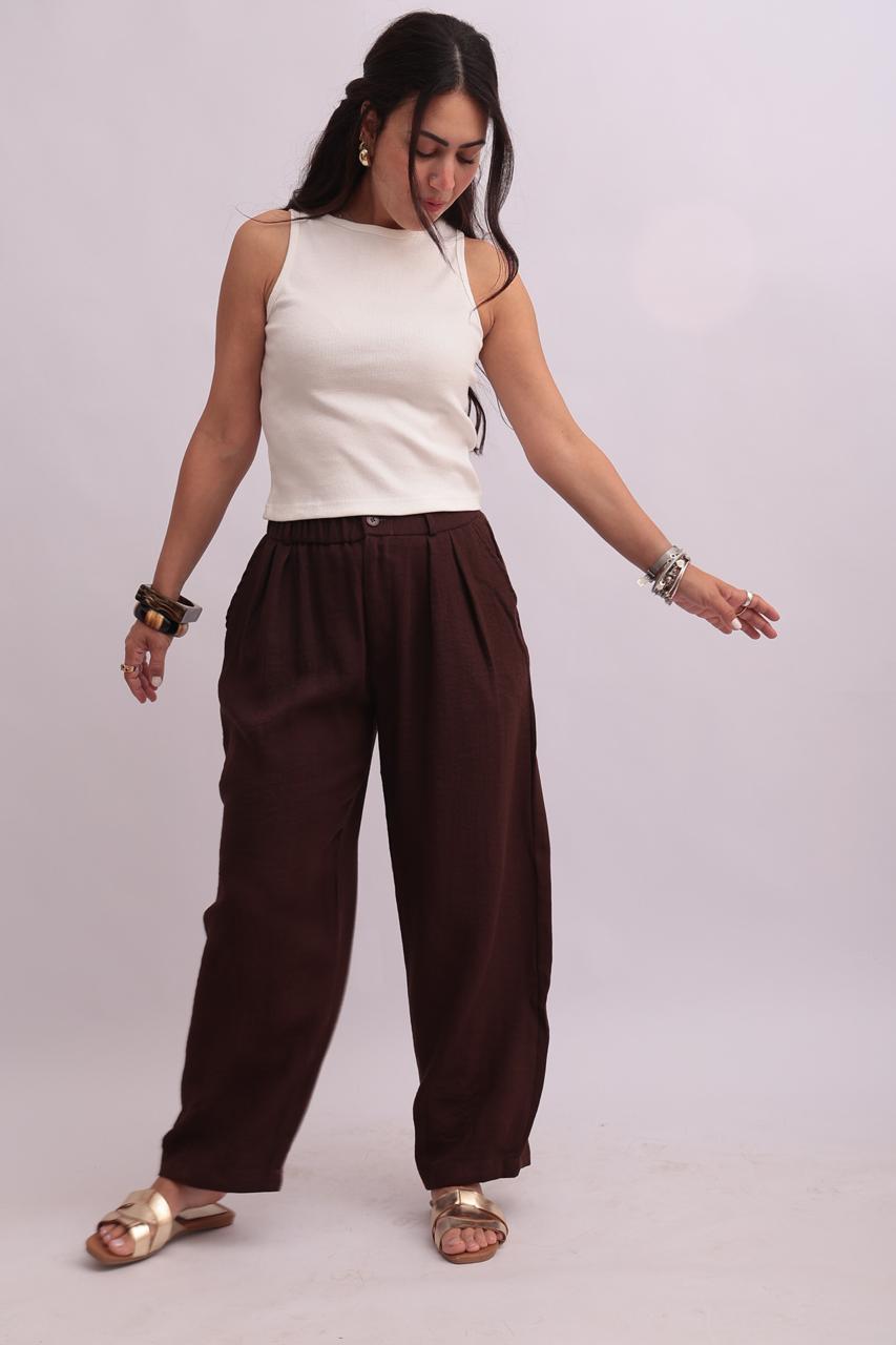 Full-body shot of a model wearing a white crop tank top styled with dark chocolate brown trousers and gold sandals.