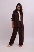 Full-body shot of a model wearing an open chocolate brown linen overshirt over a white tank top, paired with matching dark brown linen trousers.