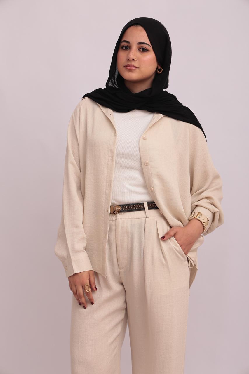 Close-up shot of a model wearing a cream linen overshirt open over a white base top, styled with cream linen trousers and a black belt.
