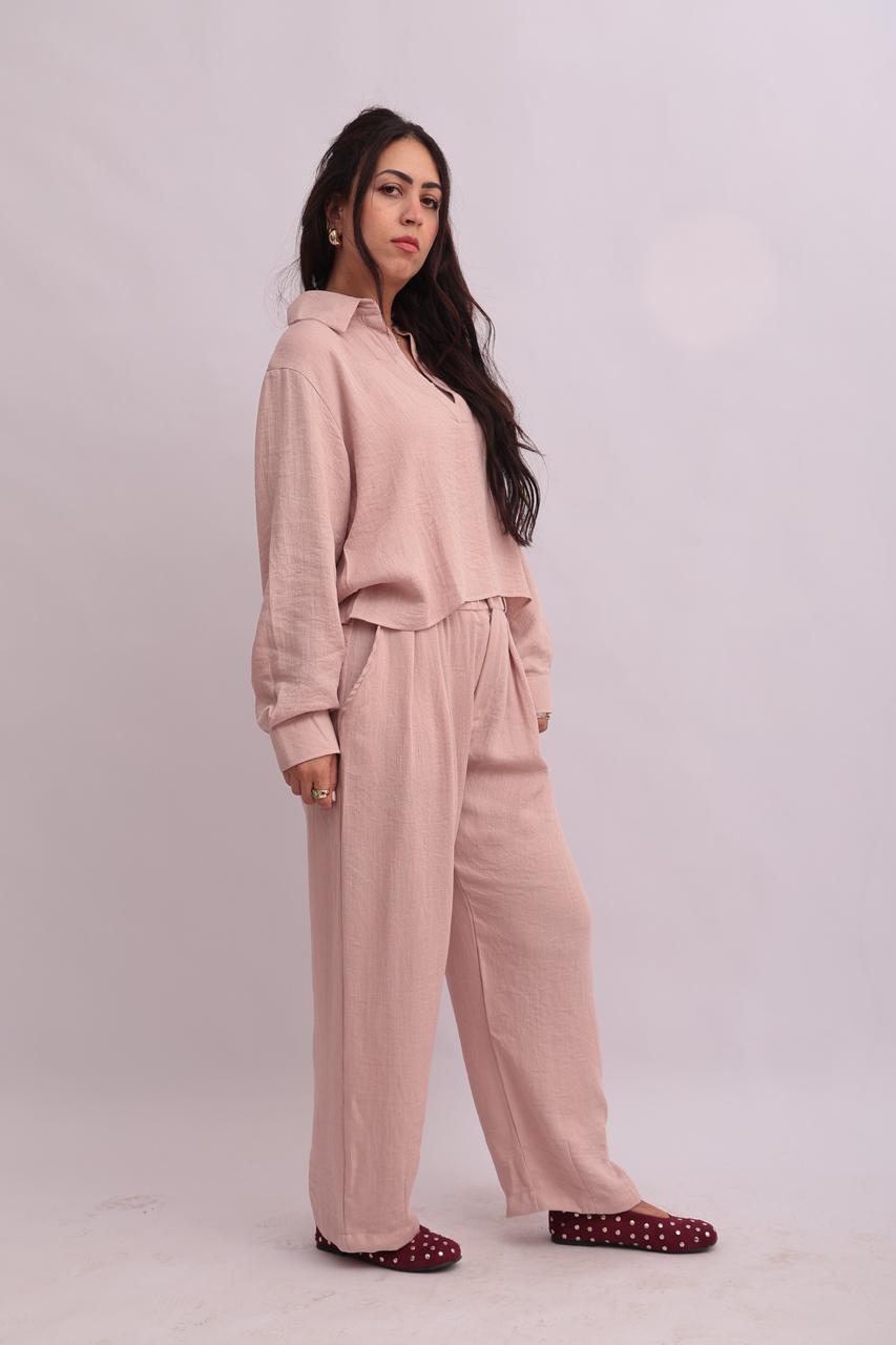 Side angle view of a model styling a matching blush pink linen set with long sleeves and relaxed pants.