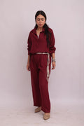 Full-body shot of a model wearing a burgundy linen shirt and matching wide-leg trousers, styled with a braided woven belt.