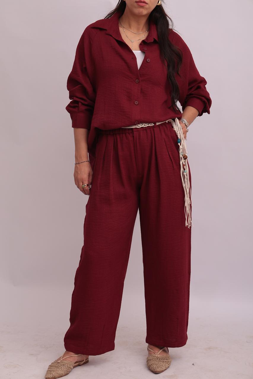 Close-up shot of a model wearing a burgundy linen shirt and matching wide-leg trousers, styled with a braided woven belt.