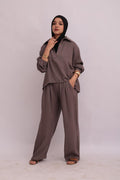 Full-body shot of a model in a black hijab wearing a taupe linen pullover collar shirt and matching wide-leg trousers.